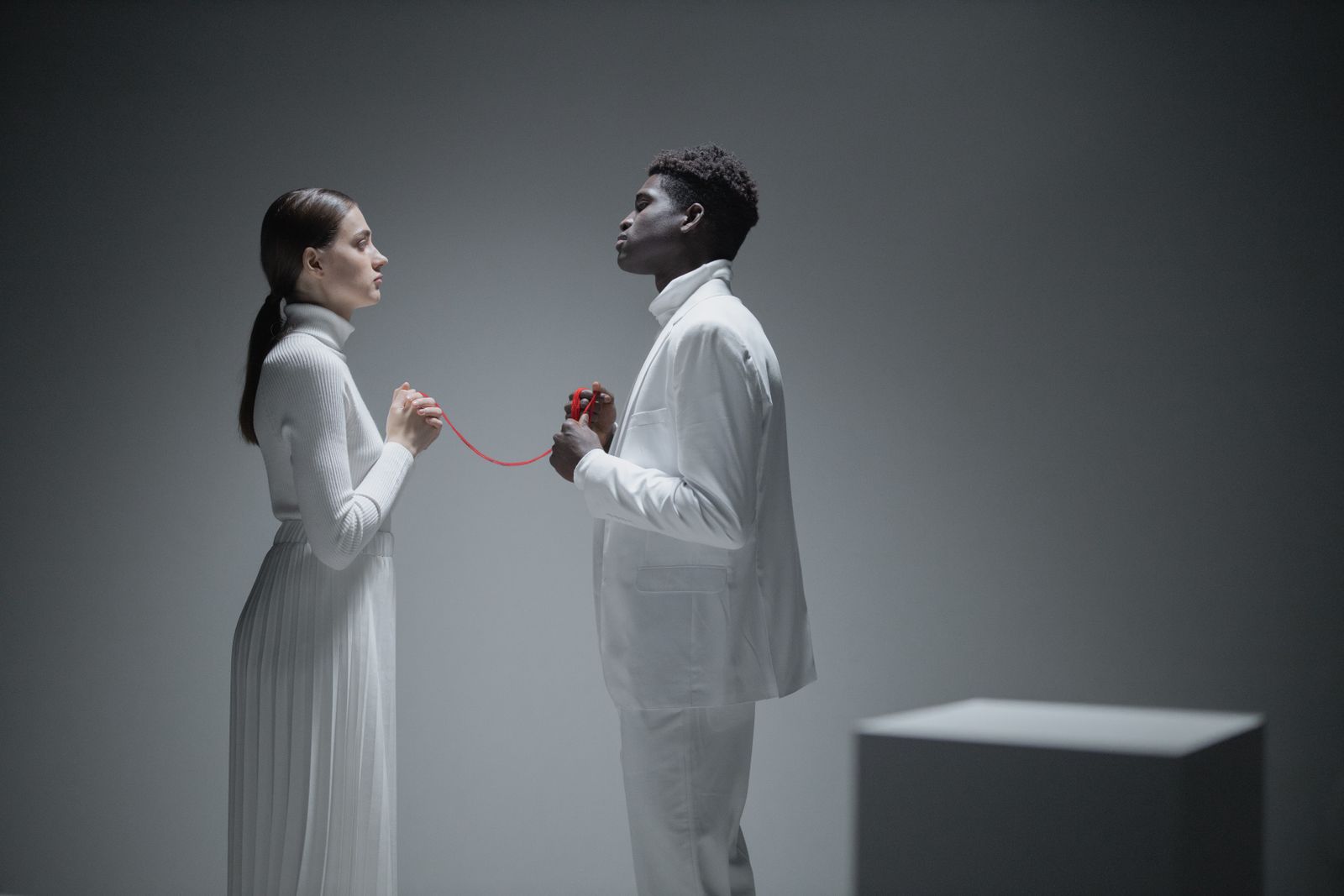 Un couple habillé en blanc relié par un fil rouge dans un studio minimaliste.